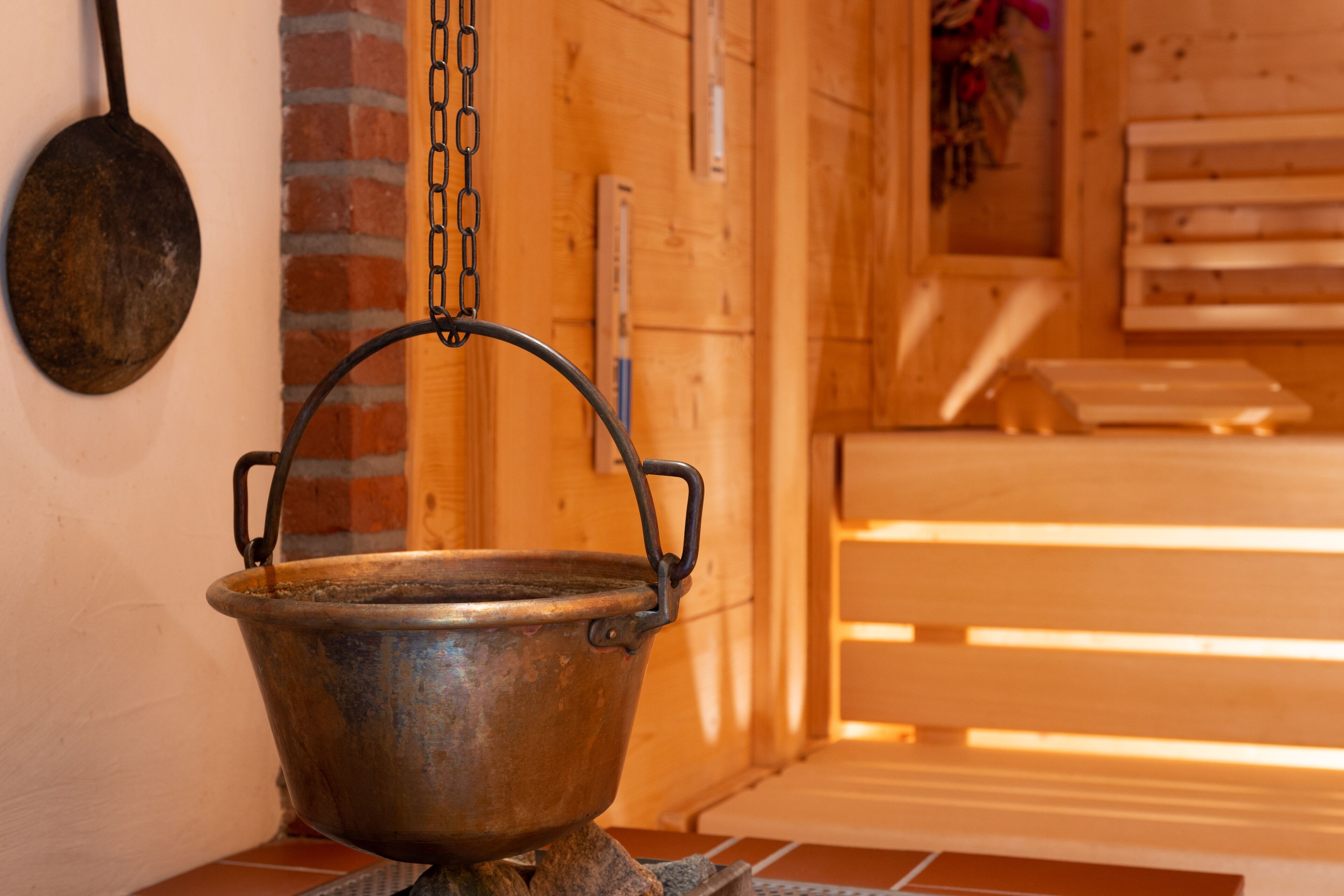 A rustic interior with a metal pot on a stove, wooden benches, and a brick wall.