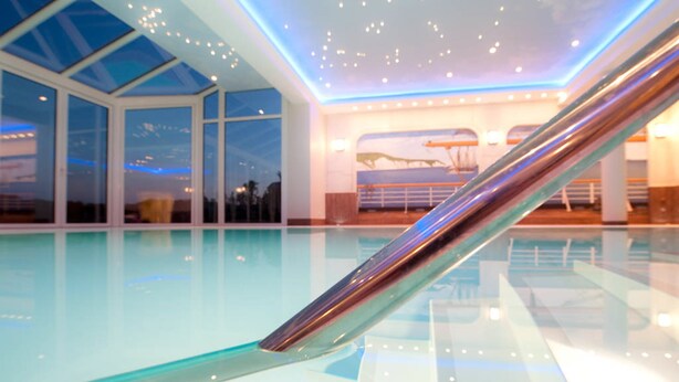 Une piscine intérieure moderne, dotée de rampes en verre et d’un plafond agrémenté de luminaires encastrés.