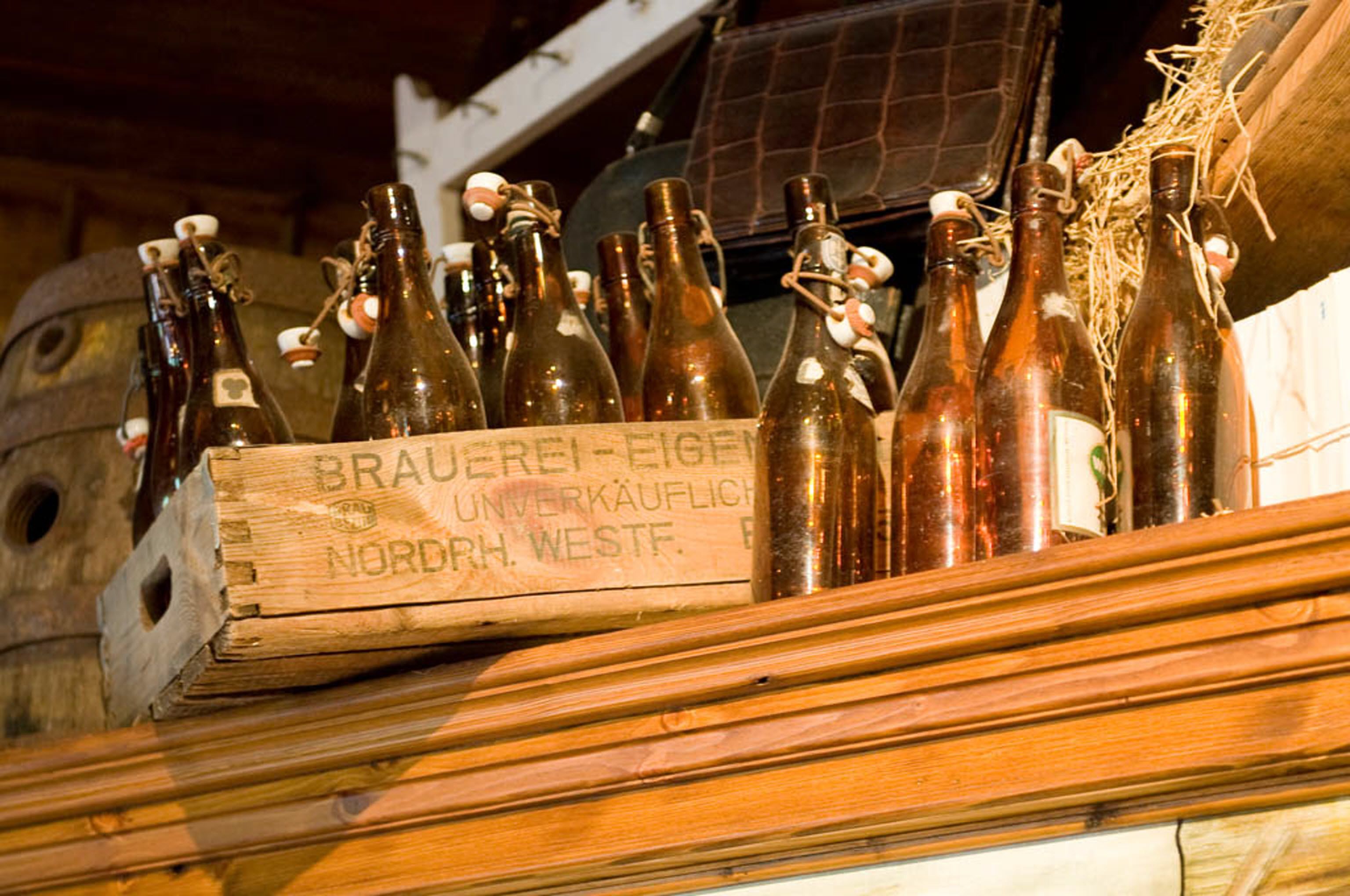 A wooden crate labeled "BRAUEREI-EIGEN UNVERKAUFLICHE NORDRH. WESTF." filled with brown glass bottles.