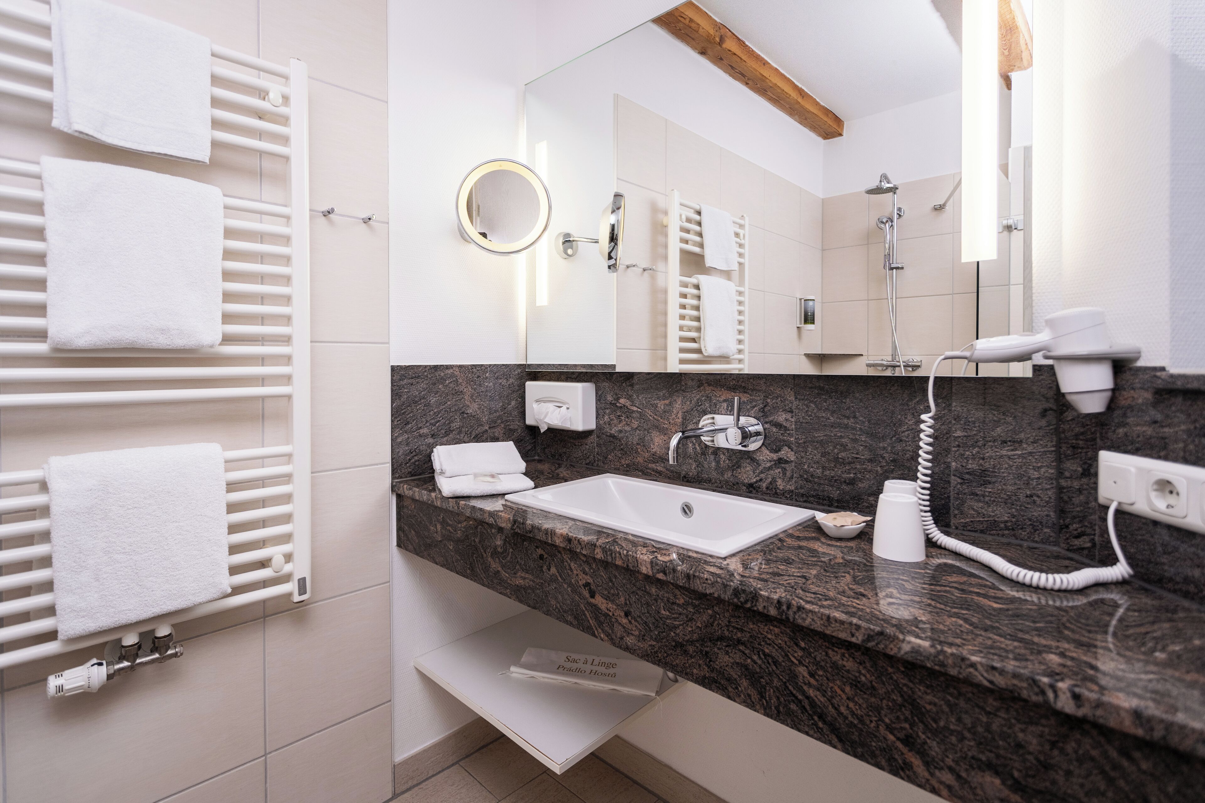 A modern bathroom with a marble countertop, a white sink, a built-in mirror, a towel rack, and a handheld showerhead.