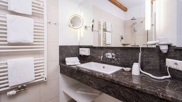 A modern bathroom with a marble countertop, a white sink, a built-in mirror, a towel rack, and a handheld showerhead.