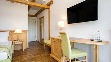 A room with a bed, a desk, a chair, a TV mounted on the wall, and a wooden floor.