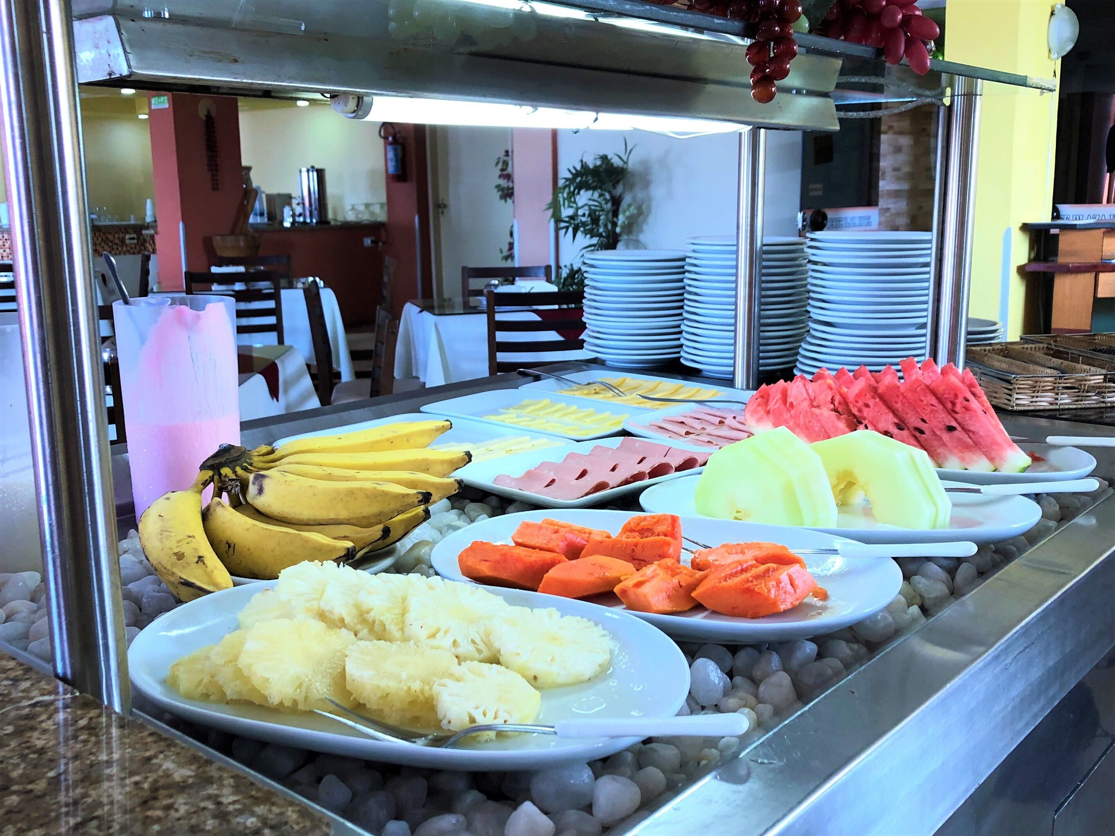 Un bufé con diversas frutas y verduras, incluyendo plátanos, sandía y zanahorias, dispuestas en platos.
