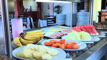 Un bufé con diversas frutas y verduras, incluyendo plátanos, sandía y zanahorias, dispuestas en platos.