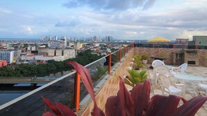 Una terraza en la azotea con vistas a un horizonte urbano, mobiliario exterior y un paraguas amarillo.