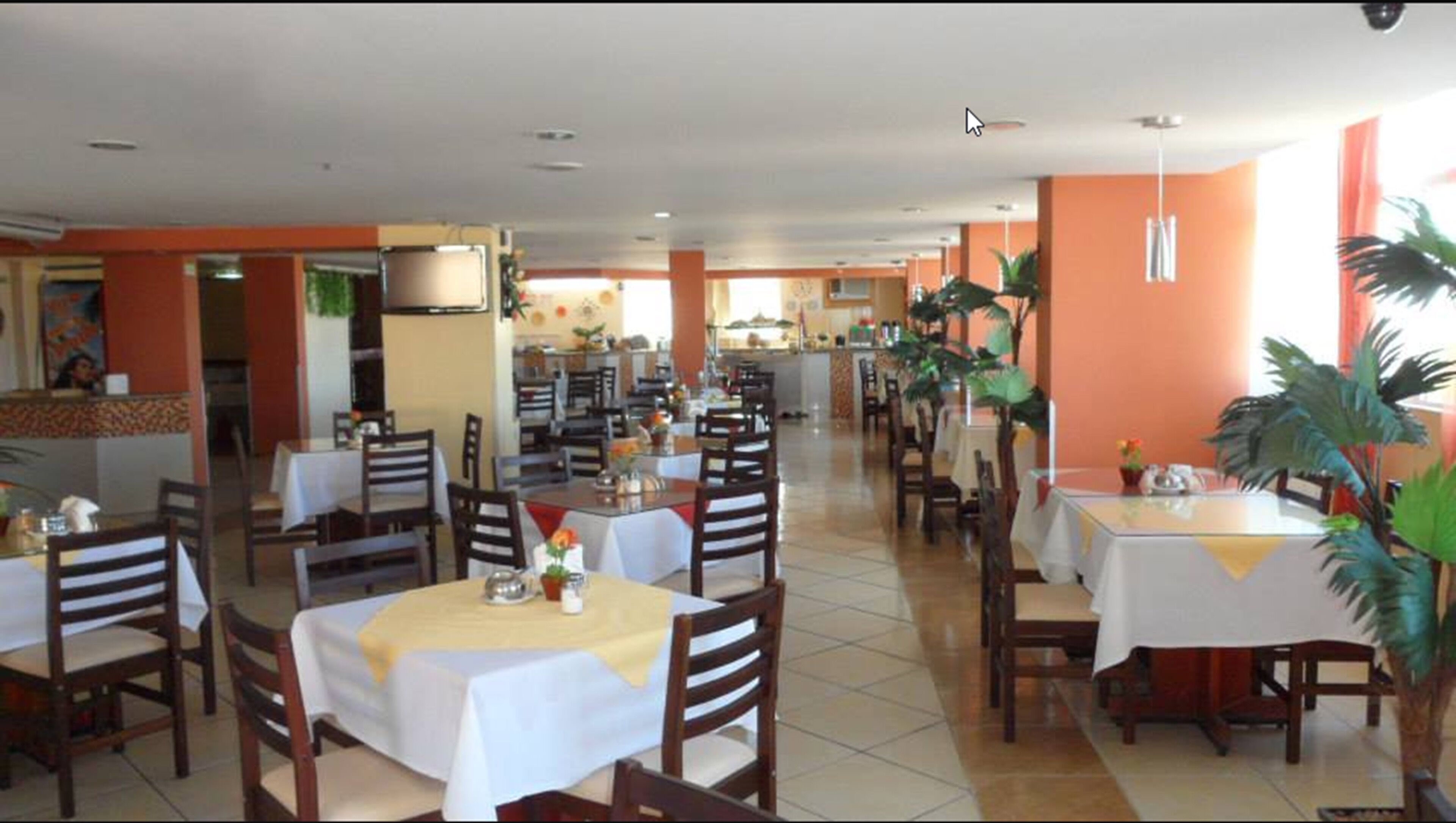 Un restaurante espacioso con numerosas mesas y sillas, suelo de baldosas y paredes anaranjadas.