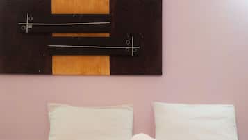 A hotel room with a bed, two pillows, a rolled towel, and a wall-mounted artwork.