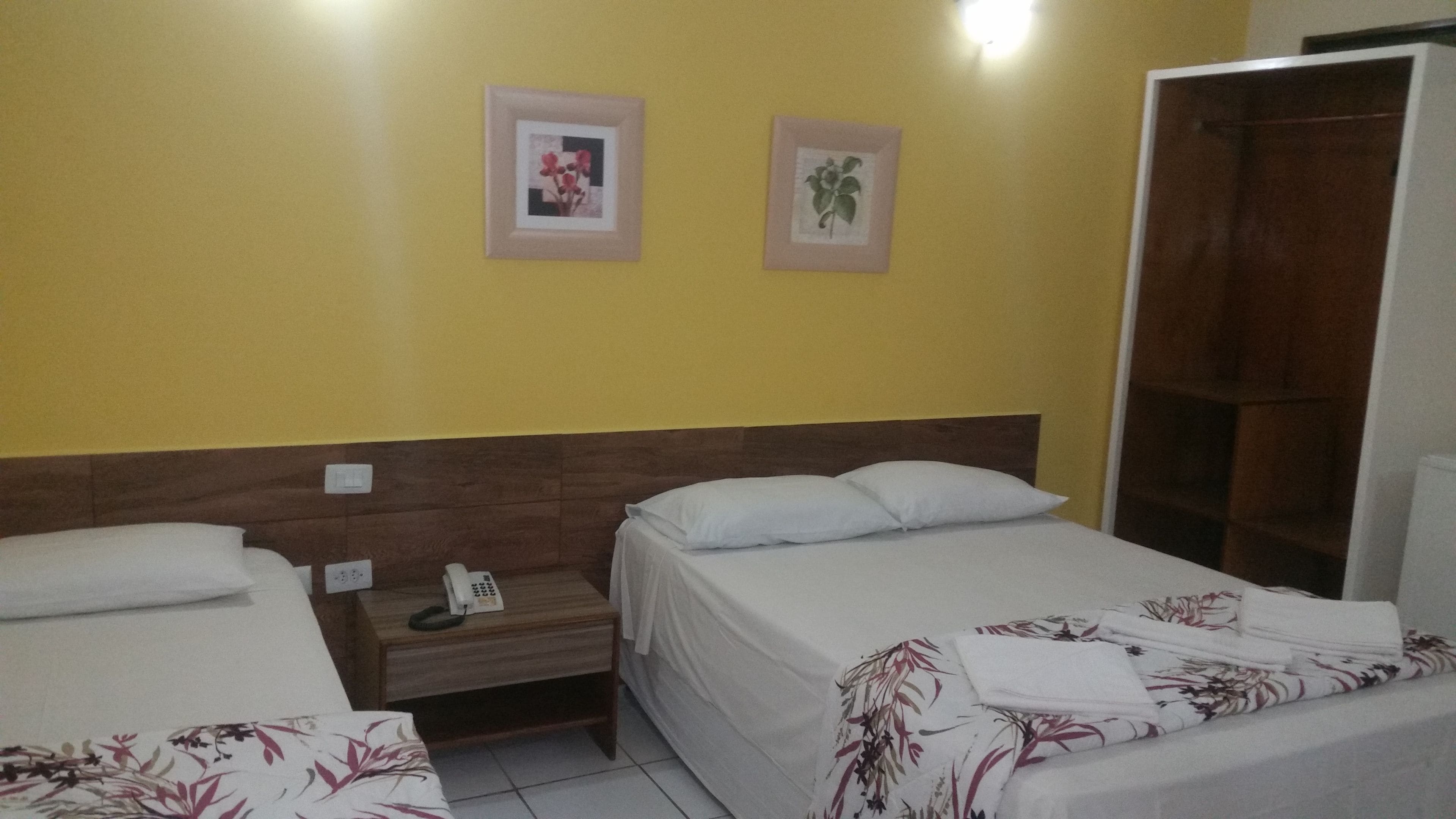 Una habitación de hotel con dos camas individuales, un cabecero de madera, una mesita de noche con un teléfono y dos cuadros enmarcados en la pared.