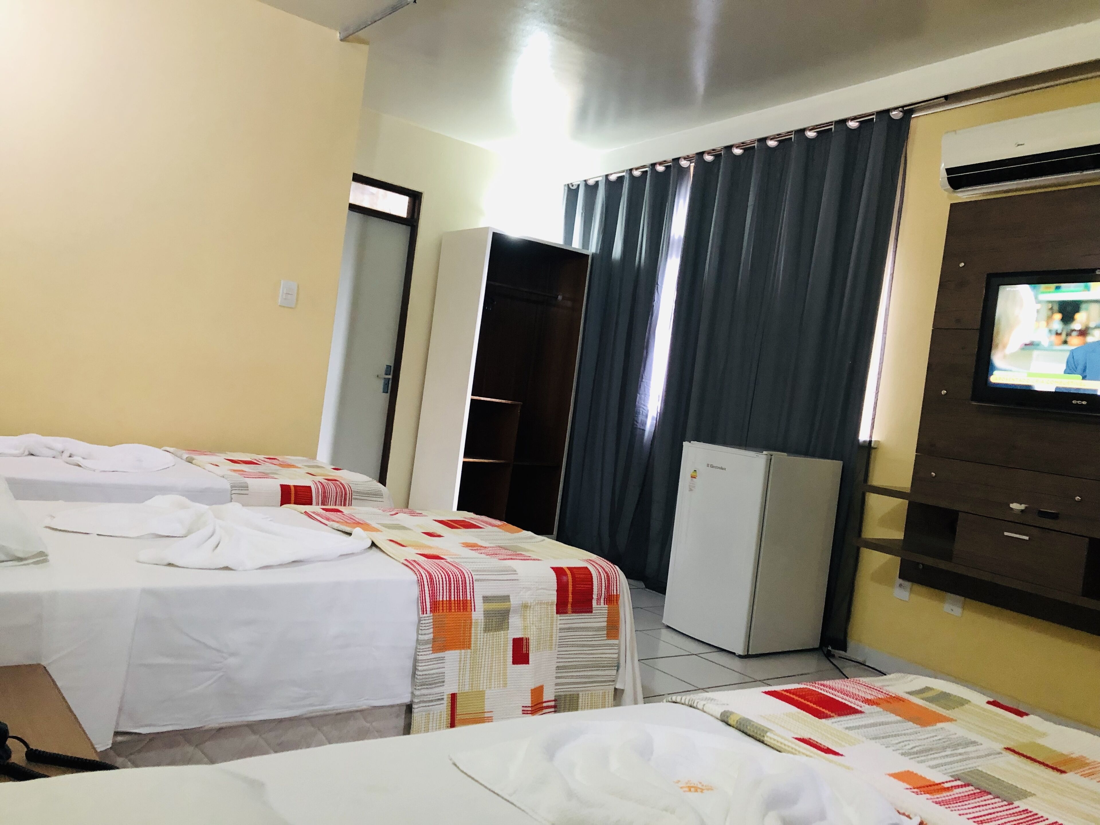 Una habitación de hotel con dos camas, televisión, refrigerador y armario.