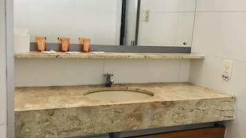 A bathroom with a large mirror, a sink, and a shelf with toiletries.