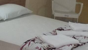 A single bed with a floral bedspread, a white pillow, and a plain wall with a framed picture.