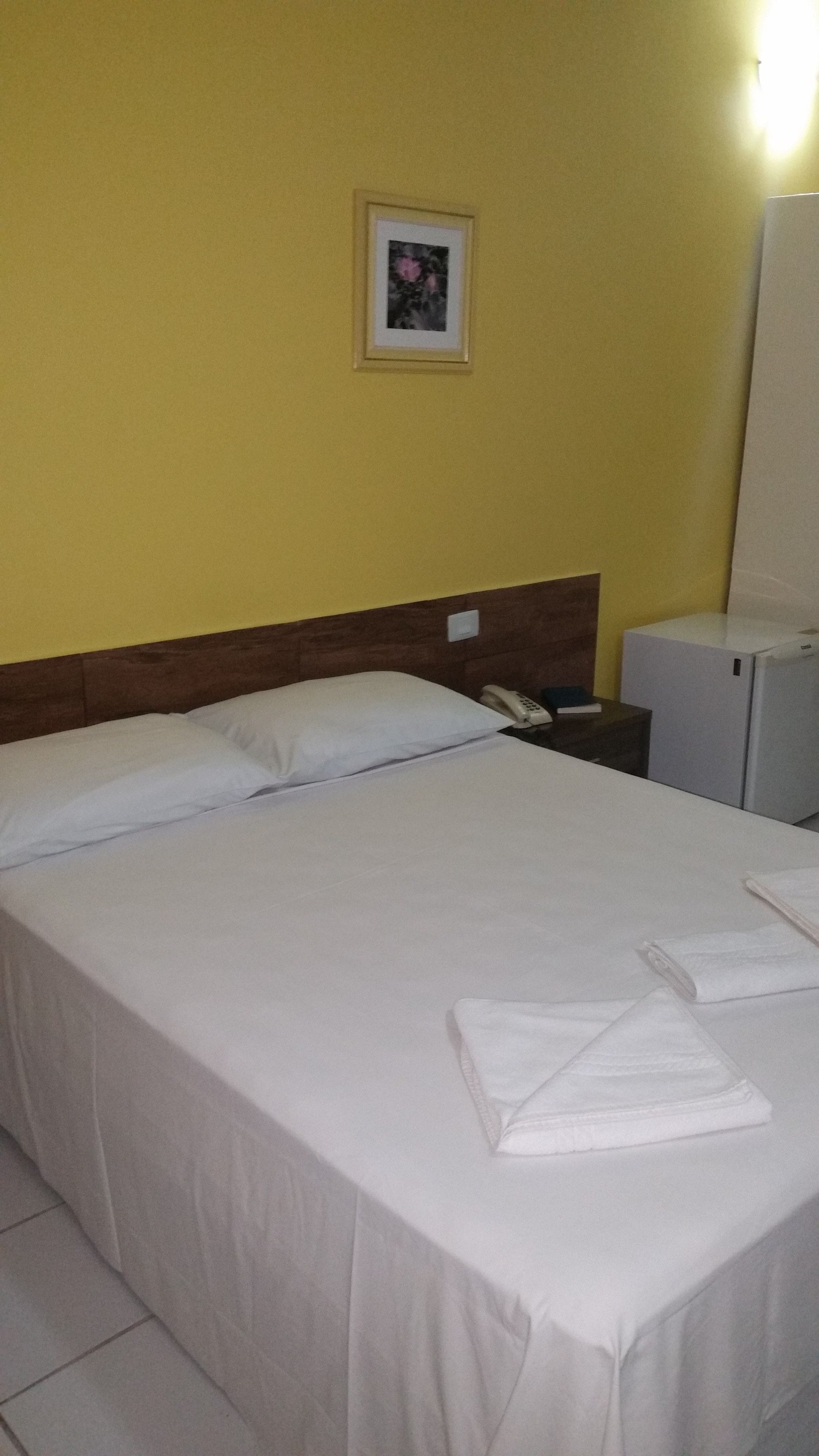 Una habitación de hotel con una cama, una mesita de noche, un teléfono y un refrigerador.