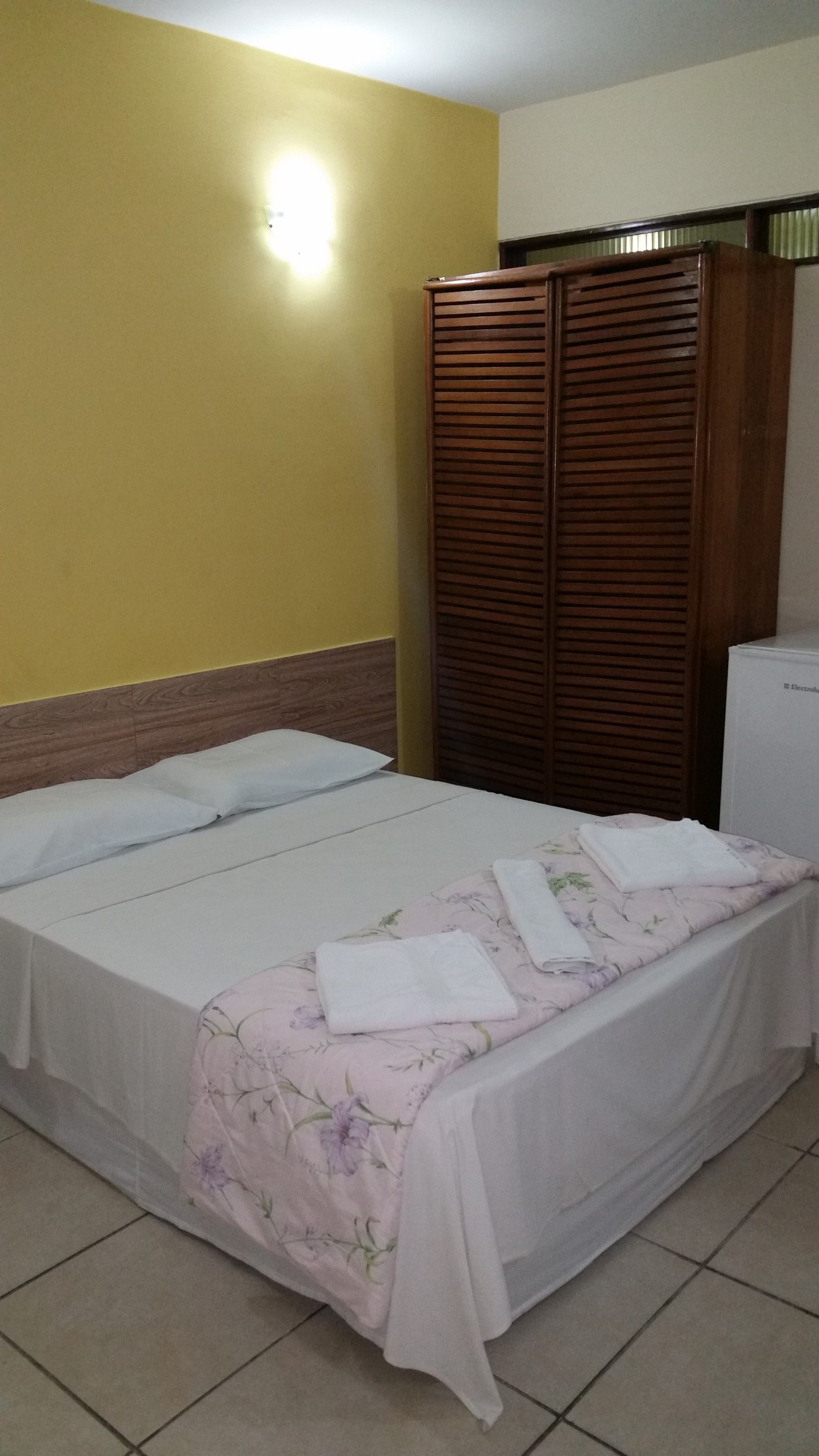 A room with a bed, a wardrobe, and a small white appliance.