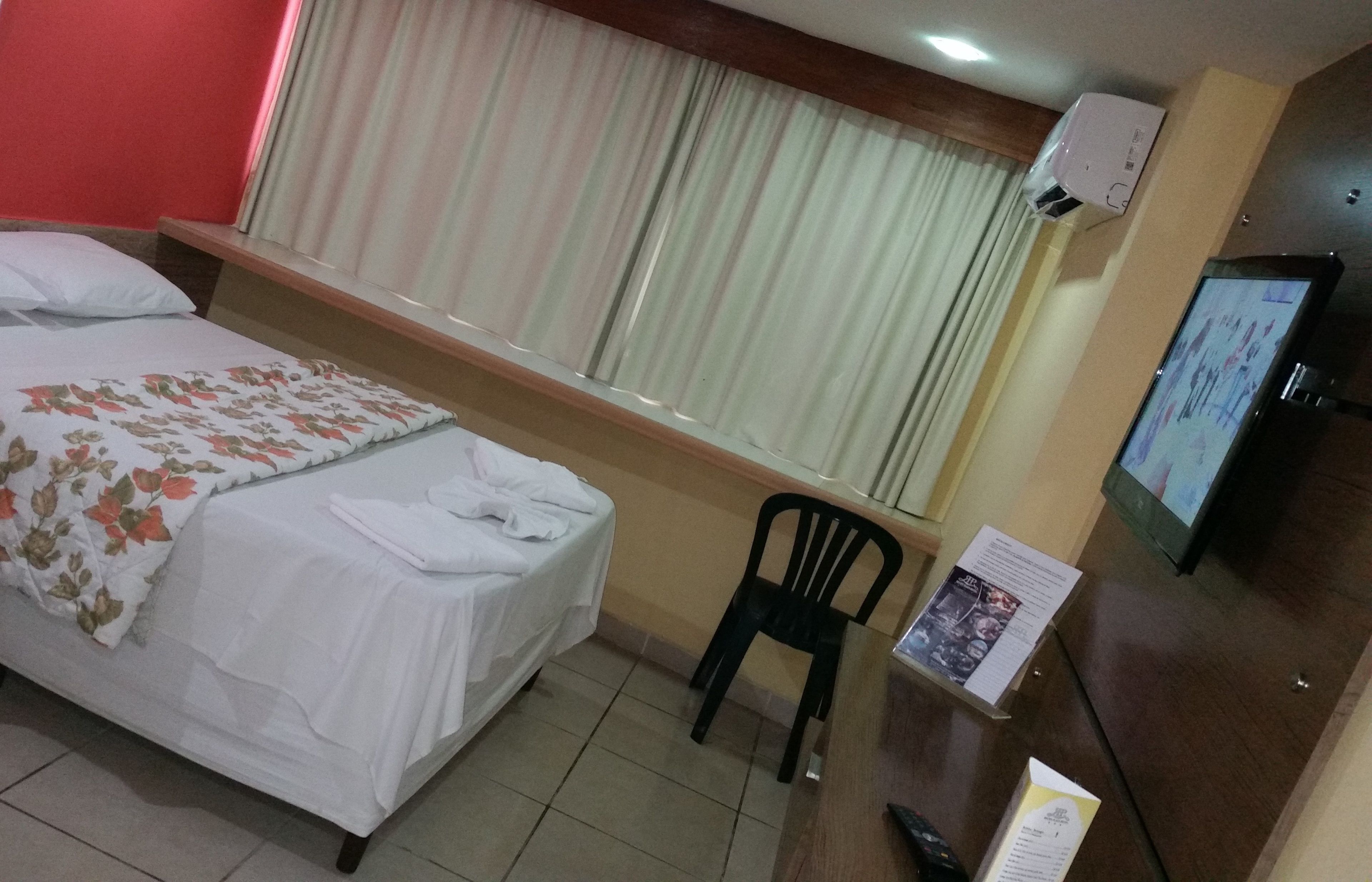 A hotel room with two beds, a desk with a chair, a television, and a window with curtains.