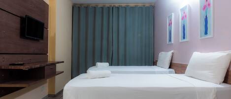 A hotel room with a bed, a TV, a window with curtains, and artwork on the wall.