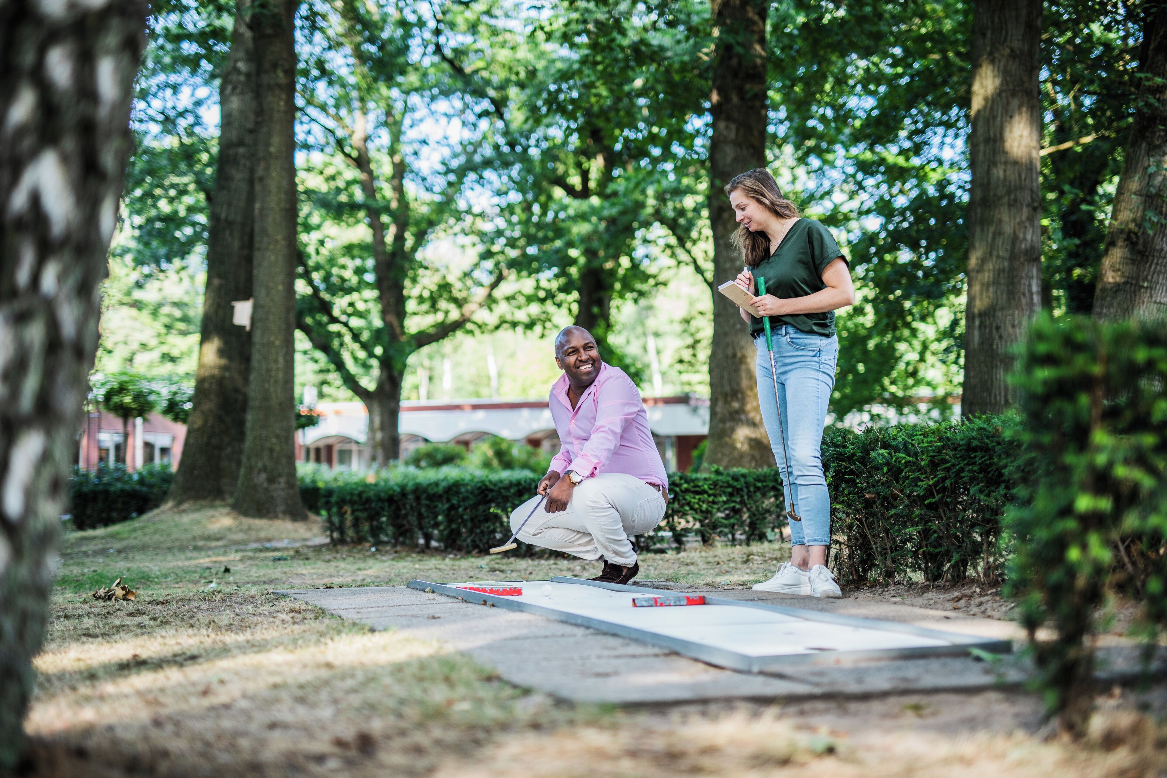 A person playing shuffleboard in an outdoor setting with trees and a paved area.