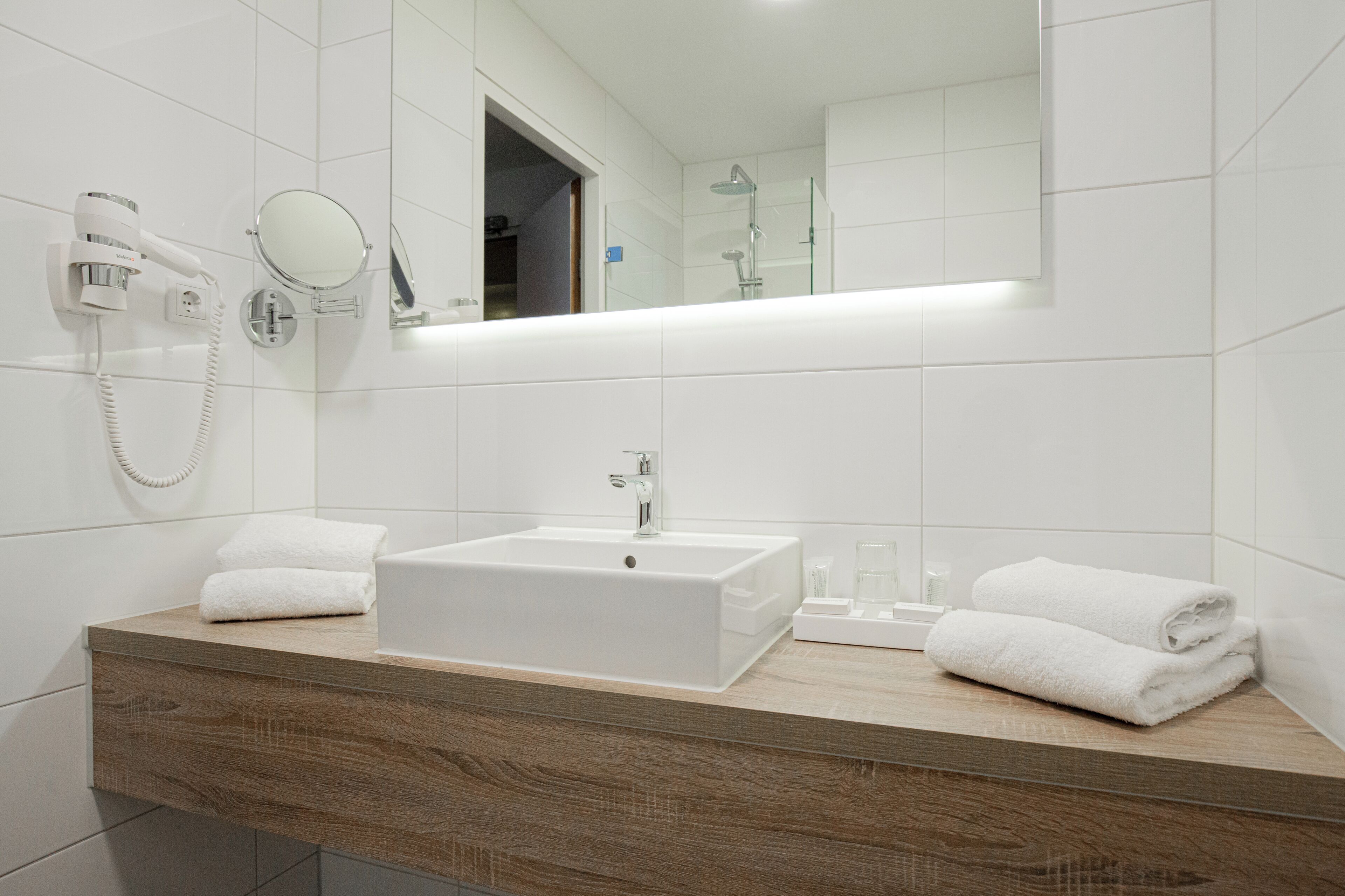 A modern bathroom with a large mirror, a hairdryer, a sink, and two towels on the counter.