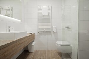 A modern bathroom with a wooden vanity, a white sink, a toilet, and a glass shower enclosure.