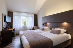Una habitación de hotel con dos camas, un escritorio con silla, televisor y ventana con cortinas.