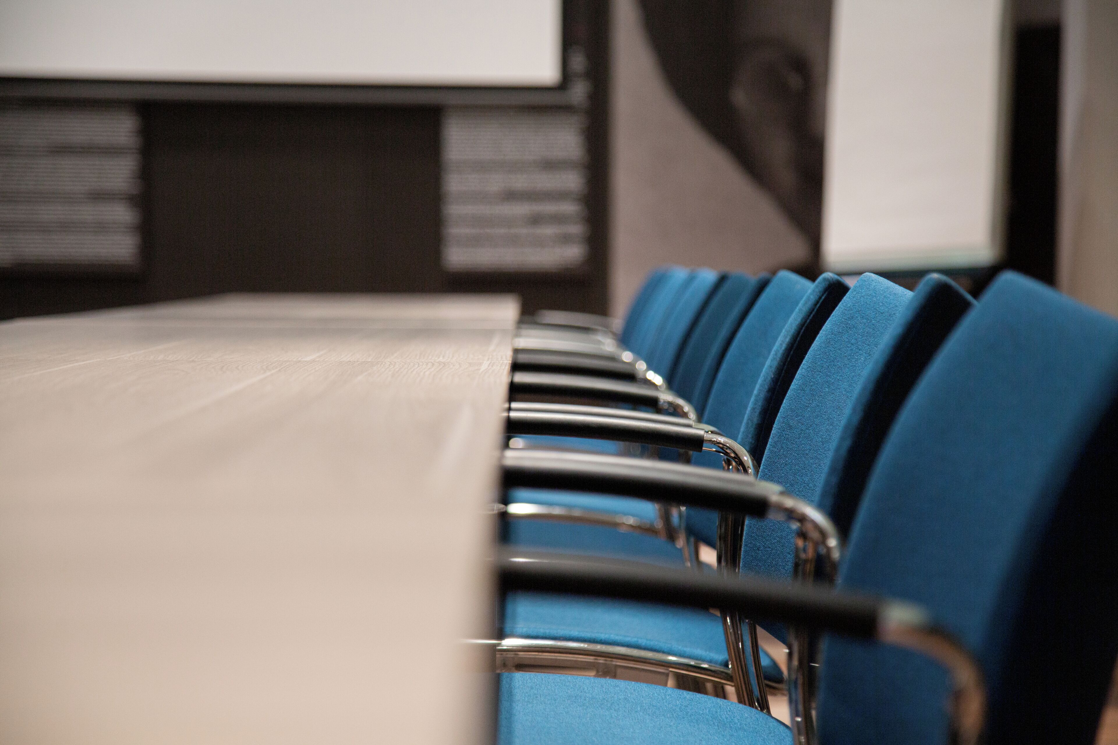 Un salón de conferencias con una larga mesa y filas de sillas azules.