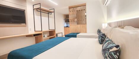 A modern hotel room with a large bed, a desk, a TV, and a kitchenette.