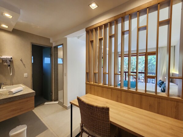 A modern bathroom with a sink, towel, and hairdryer. There is a wooden partition with a window overlooking a balcony.