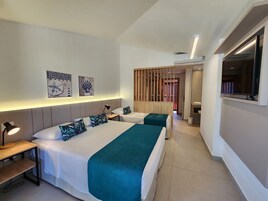 Quarto de hotel com duas camas, uma escrivaninha, uma lâmpada e obras de arte na parede.