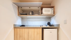 A compact kitchenette with a microwave, kettle, and coffee maker on a countertop, and a small refrigerator. - Blu Smart Stay (Búzios)