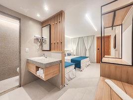 Habitación de hotel con tocador de madera, cama con ropa de cama azul, un espejo grande y una puerta de madera.