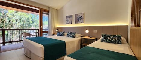 Habitación de hotel con dos camas, un balcón con vista a árboles y una mesita con lámpara.