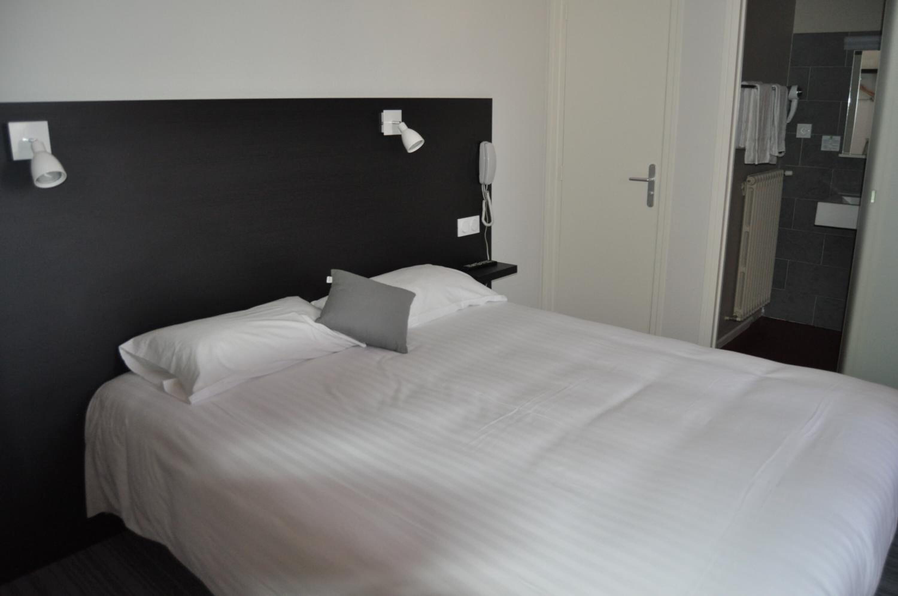 A neatly made bed with white linens and a gray pillow in a hotel room.