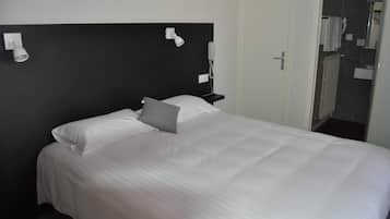 A neatly made bed with white linens and a gray pillow in a hotel room.