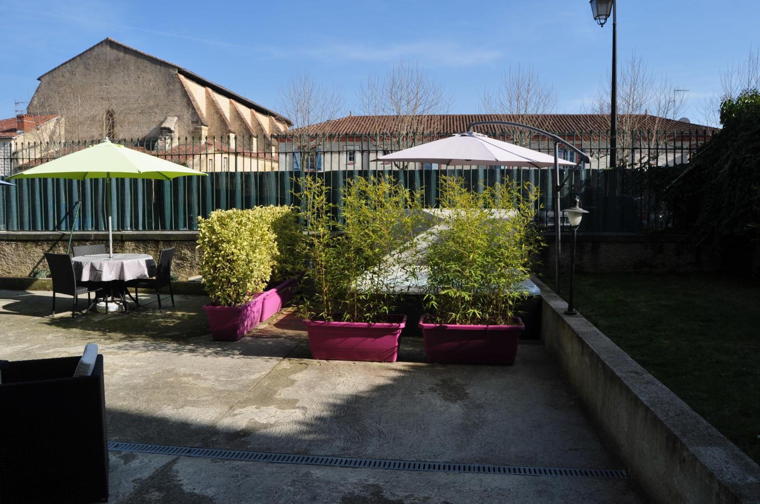 An outdoor patio area with tables and chairs, surrounded by potted plants and umbrellas.