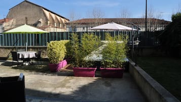 An outdoor patio area with tables and chairs, surrounded by potted plants and umbrellas.