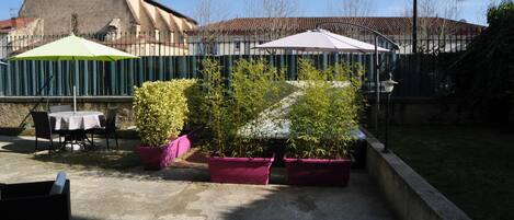 Un patio al aire libre con mesas y sillas, rodeado de macetas con plantas y sombrillas.