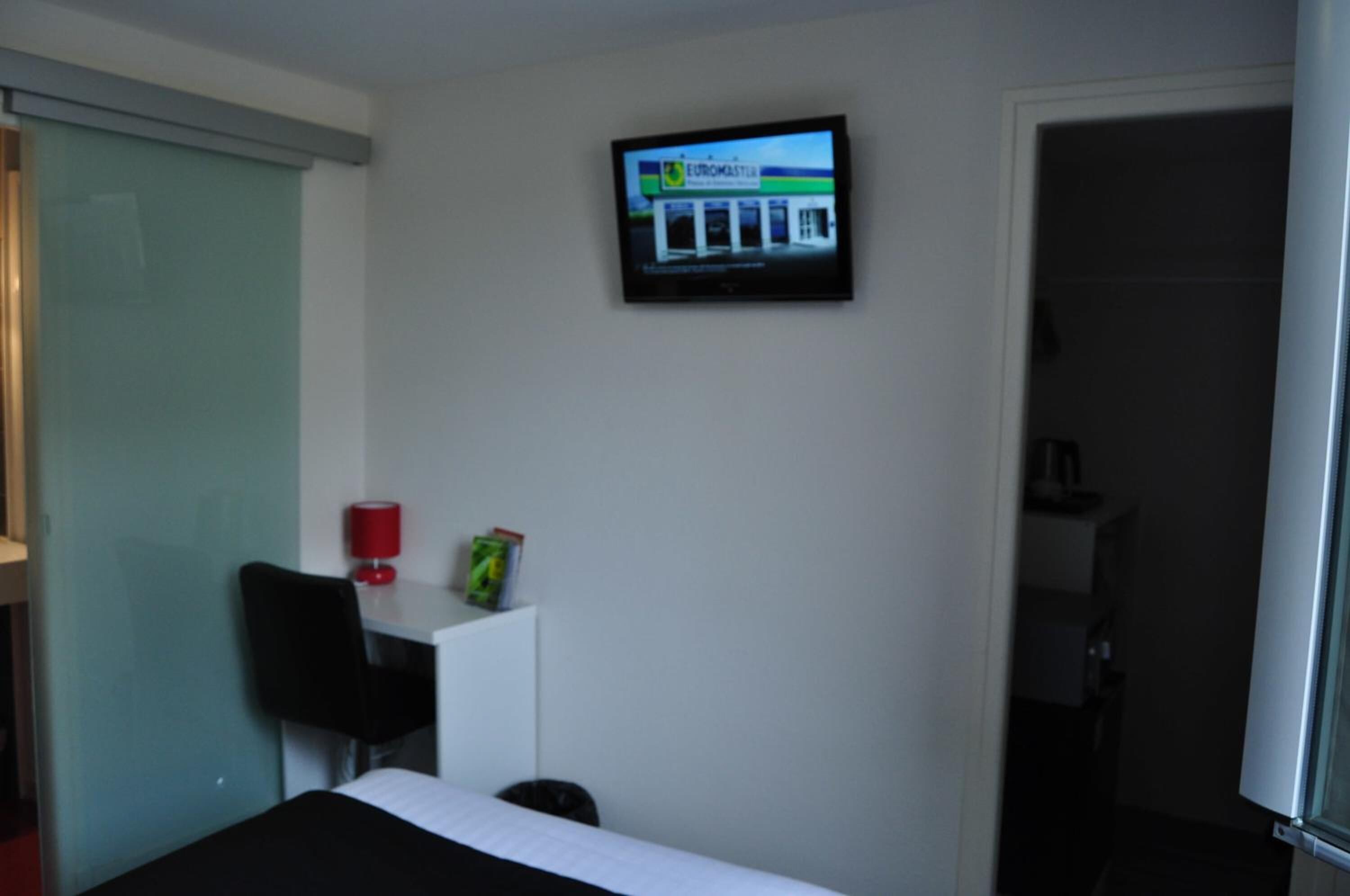 A hotel room with a bed, a desk, a chair, a television mounted on the wall, and a door leading to the bathroom.