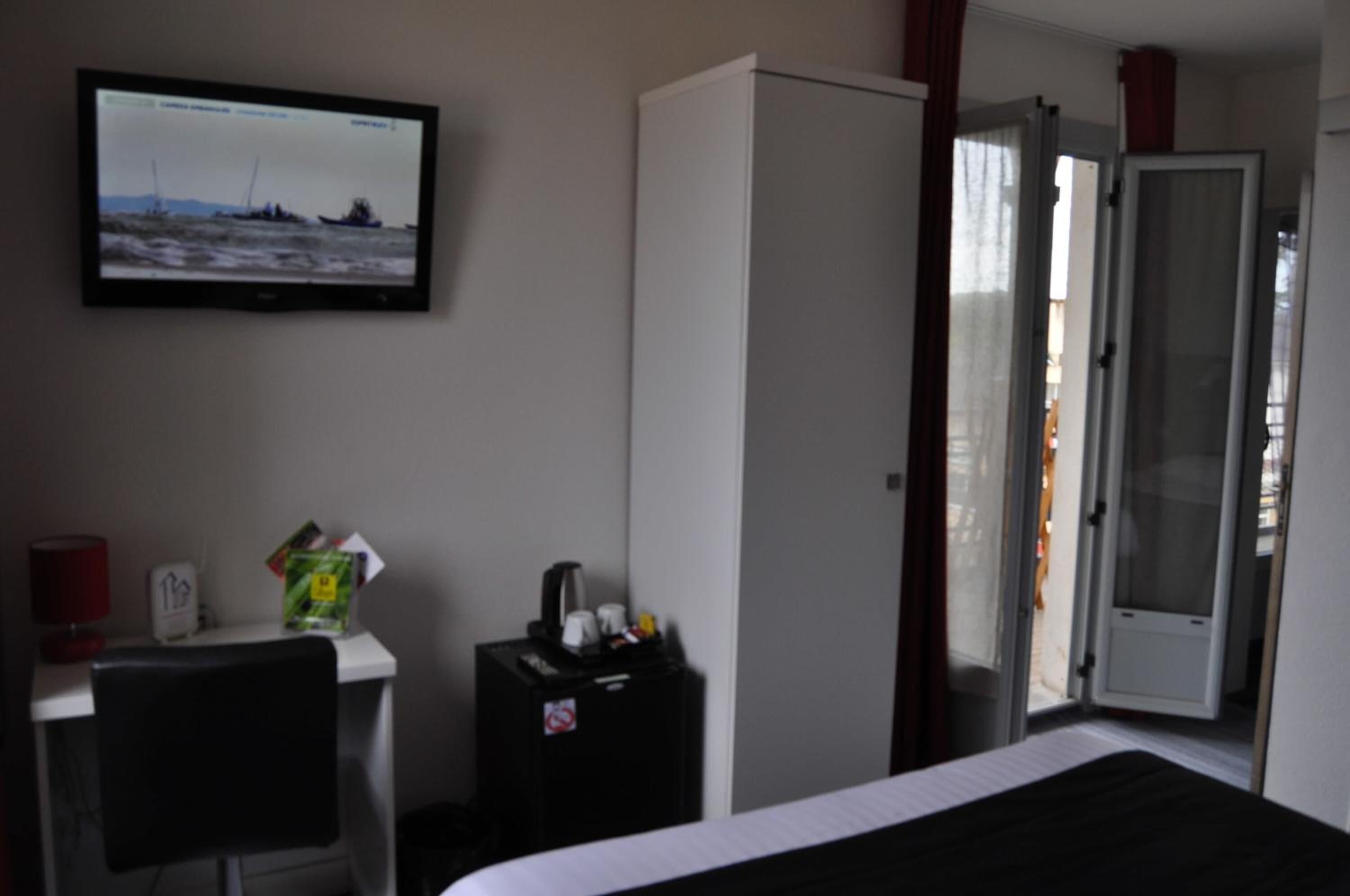 Habitación de hotel con cama, escritorio con monitor de computadora, armario y puerta que da a un área exterior.