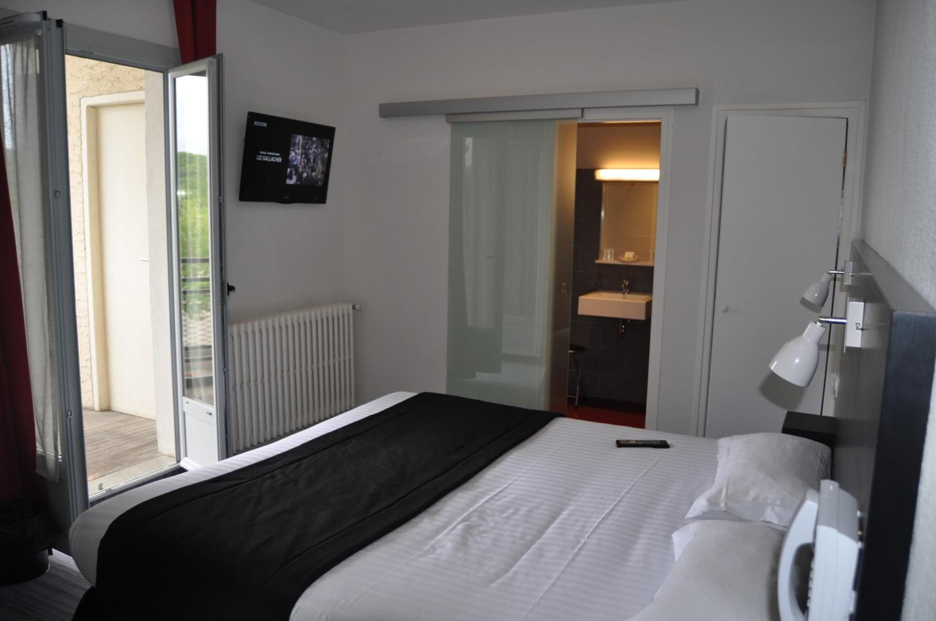Habitación de hotel con cama, televisor, baño con espejo y puerta corrediza a un balcón.