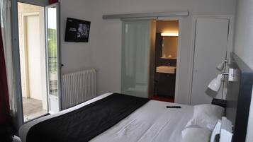 Habitación de hotel con cama, televisor, baño con espejo y puerta corrediza a un balcón.