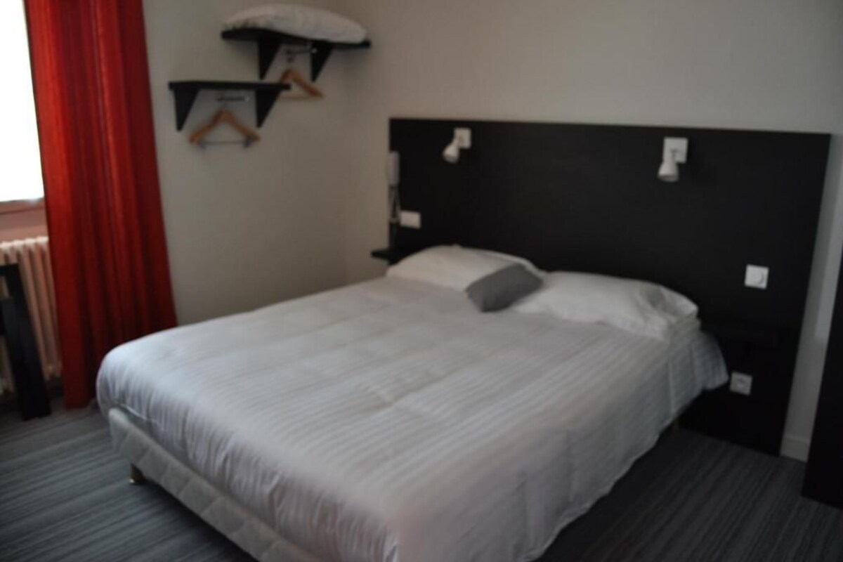 Una habitación de hotel con una cama grande, un cabecero y una estantería fijada a la pared.