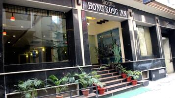 The exterior of the Hong Kong Inn hotel with a staircase leading to the entrance, potted plants, and a large window reflecting the Statue of Liberty.