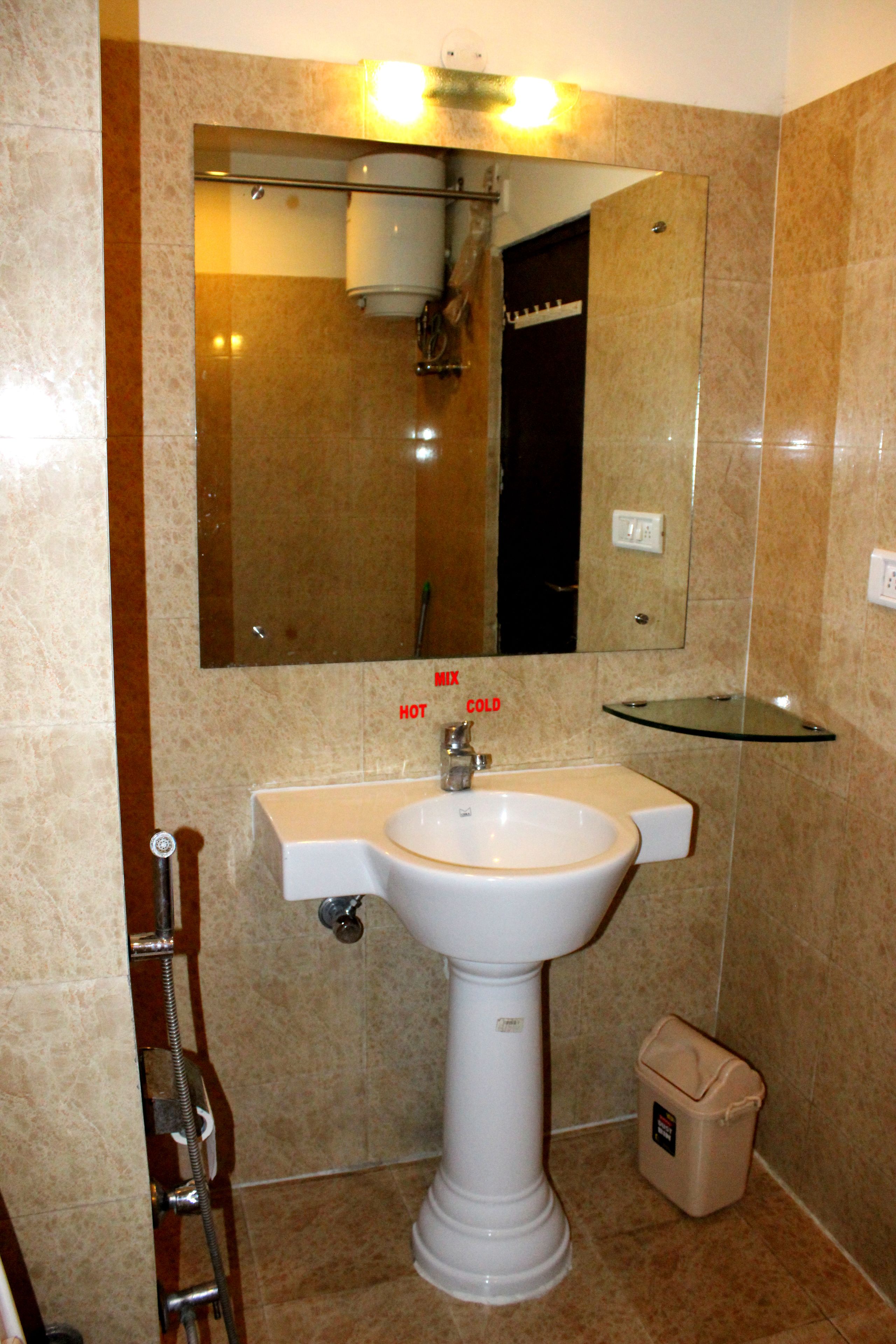 A bathroom with a white pedestal sink, a glass shelf above the sink, a mirror above the sink, and a showerhead above the mirror.