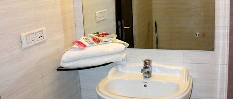 A bathroom with a white sink, mirror, and tiled walls. There is a towel rack with towels and a small trash bin.