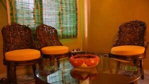 A room with two ornate wooden chairs with cushioned seats, a glass coffee table with a decorative bowl, and a window with blinds. - Hotel Hong Kong Inn (Amritsar)