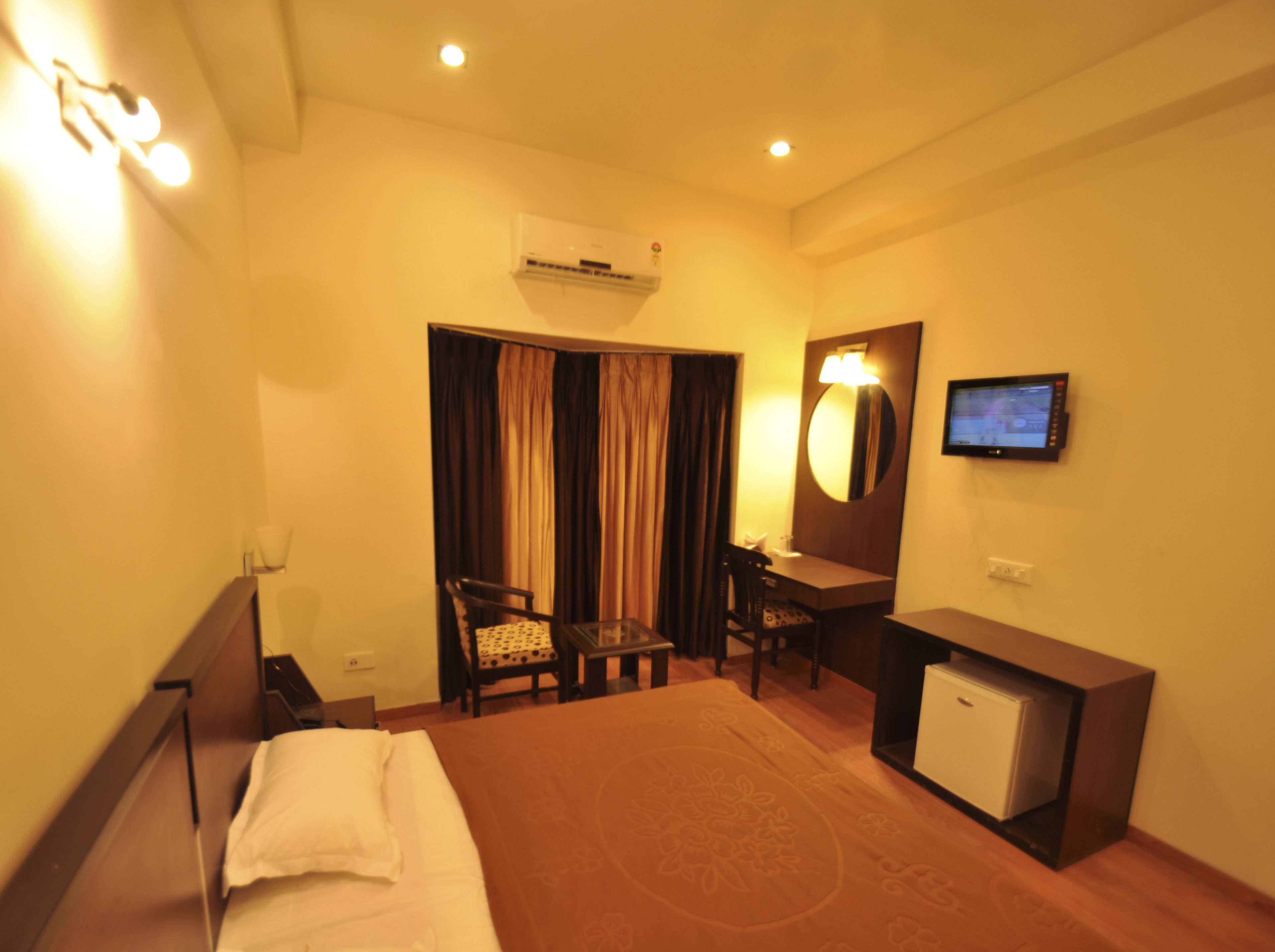 A hotel room with a bed, a desk, a chair, a television, and an air conditioning unit.