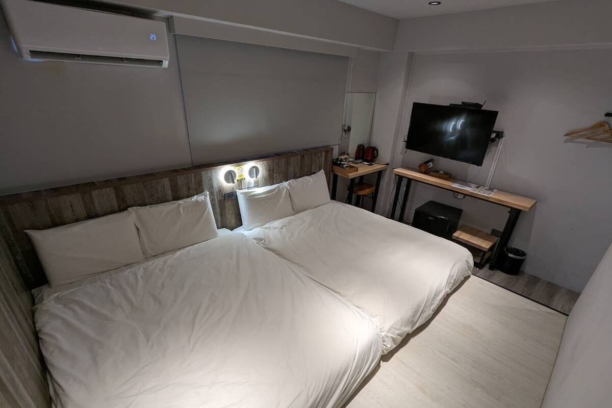 Habitación de hotel con una cama grande, un escritorio con televisor de pantalla plana, un espejo y un cesto de basura pequeño.