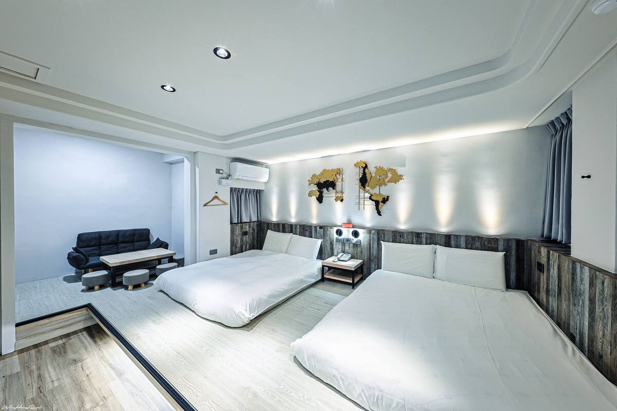 Una habitación de hotel moderna con dos camas, un sofá, una mesita y un teléfono en la pared.