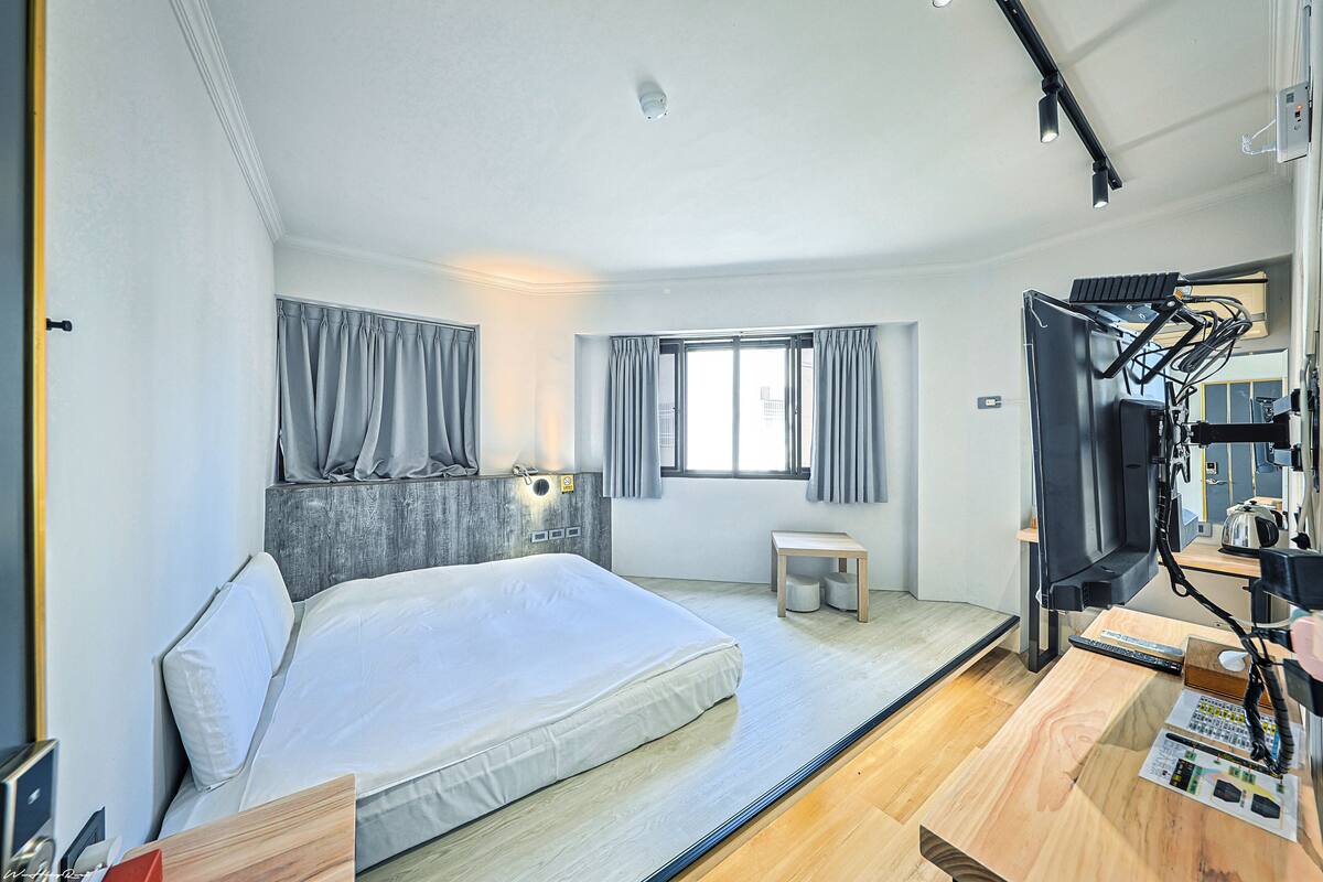 Una habitación de hotel moderna con una cama grande, un escritorio con una computadora, un televisor y una ventana con cortinas.