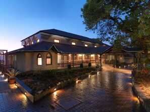 A large, two-story building with a covered patio area, surrounded by potted plants and a brick pathway. - Regenta MPG Club (Mahabaleshwar)