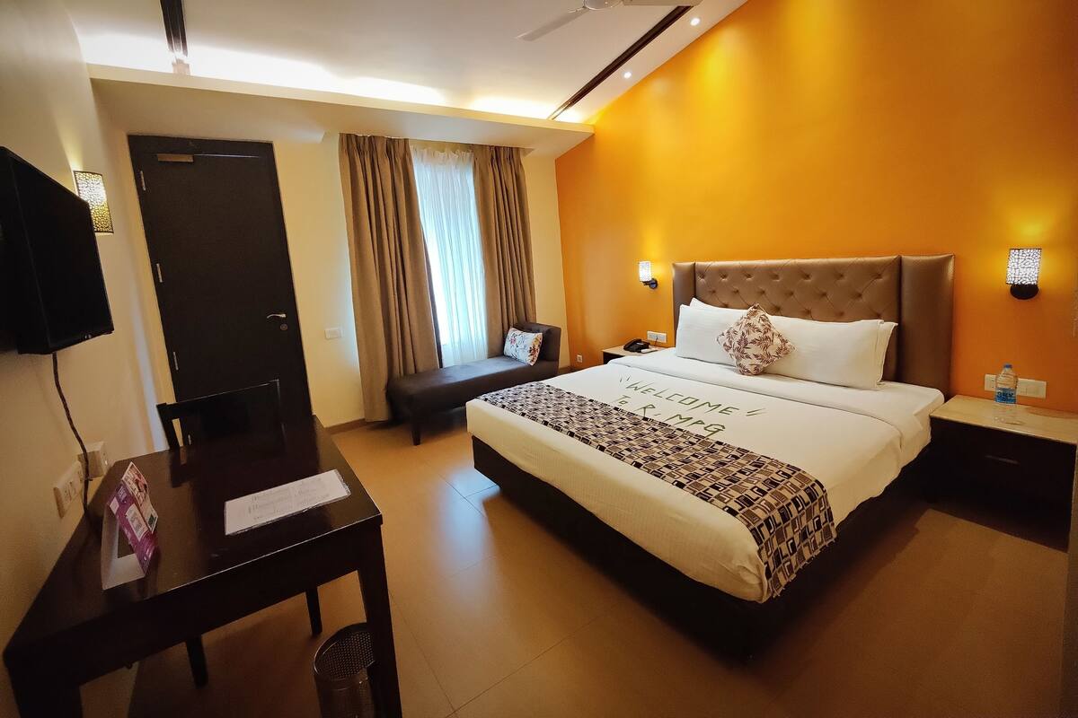 A hotel room with a large bed, a desk, a chair, a TV, and a window with curtains.